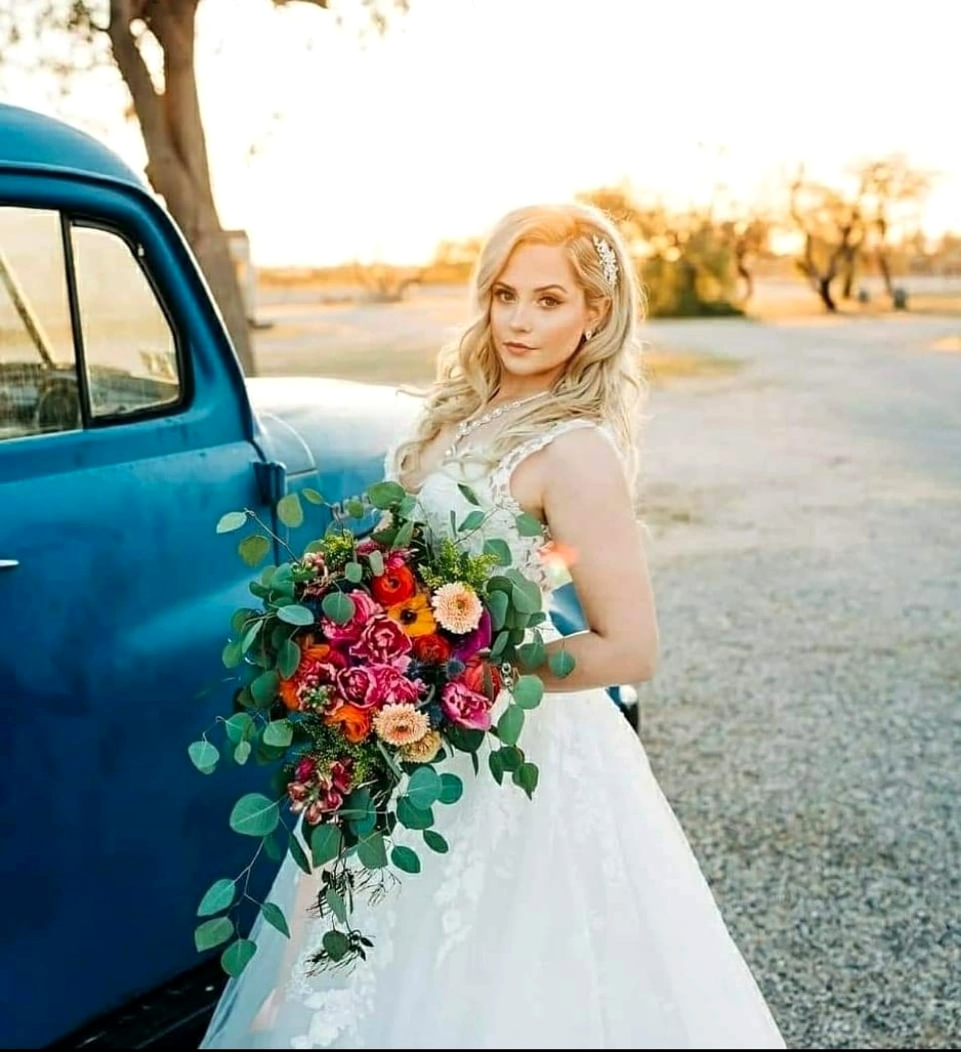 A bride with a bouquet beside a vintage pickup truck at sunset.
